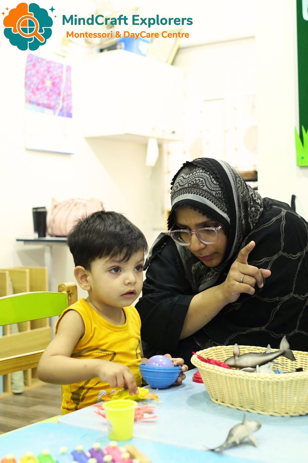 A teacher guiding a toddler at the activity table