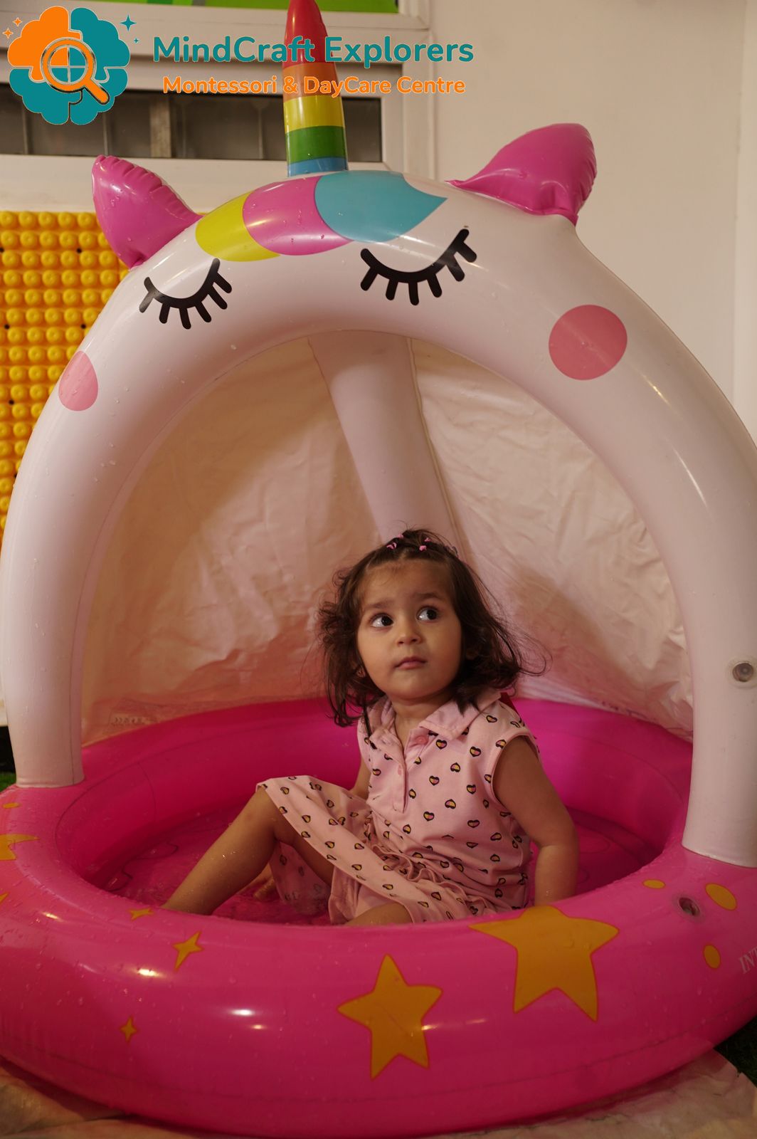 A little girl sitting in a unicorn paddling pool